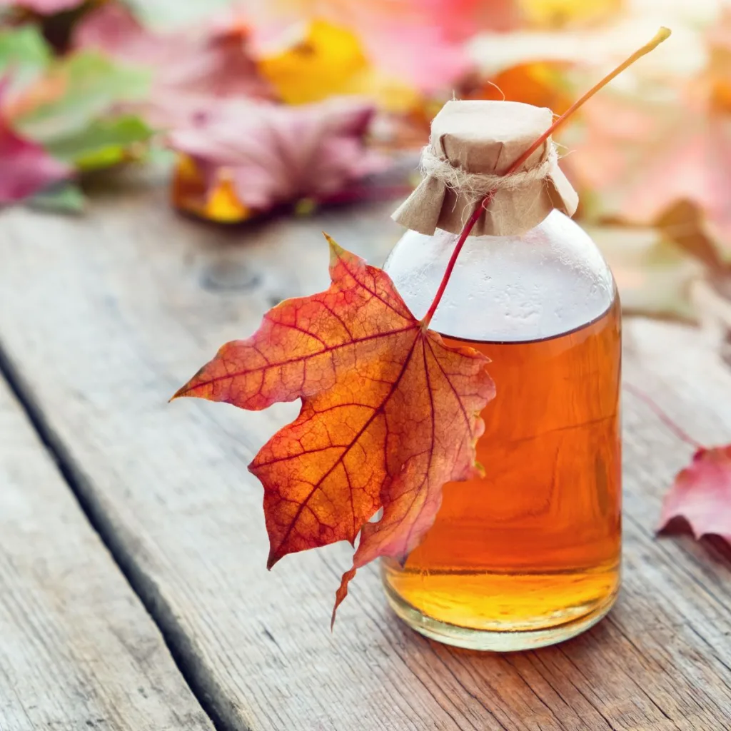 A small jar of Vermont maple syrup with maple leaves surrounding it