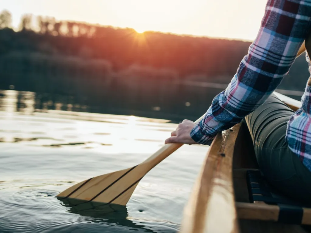 A woman sitting in a canoe on the water with her oar in the water